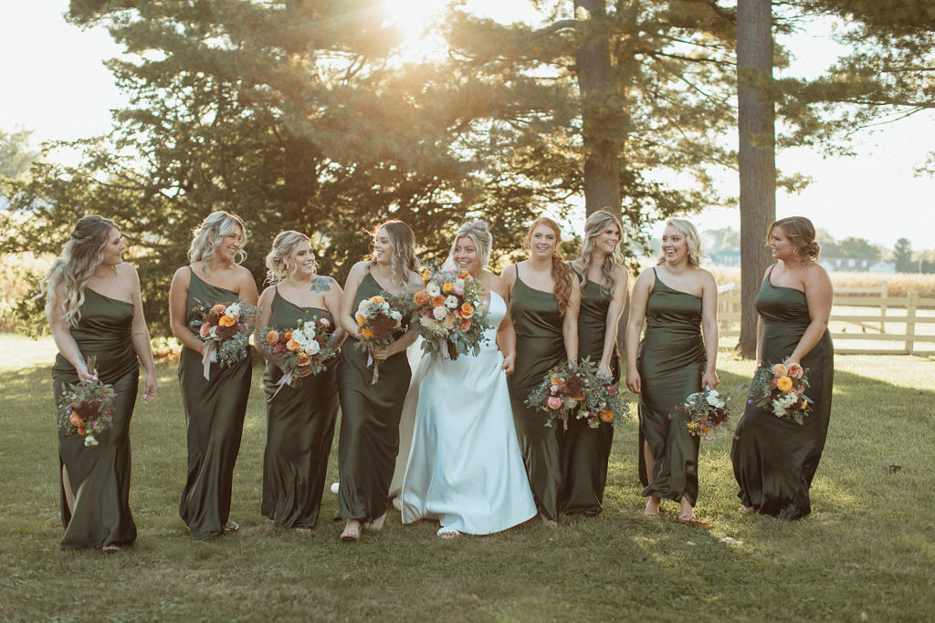 green bridesmaids dresses for a fall wedding with bridesmaids and bride walking together through lawn at sunset Wedding at Bowling Brook Mansion photographed by Charlottesville wedding photographer