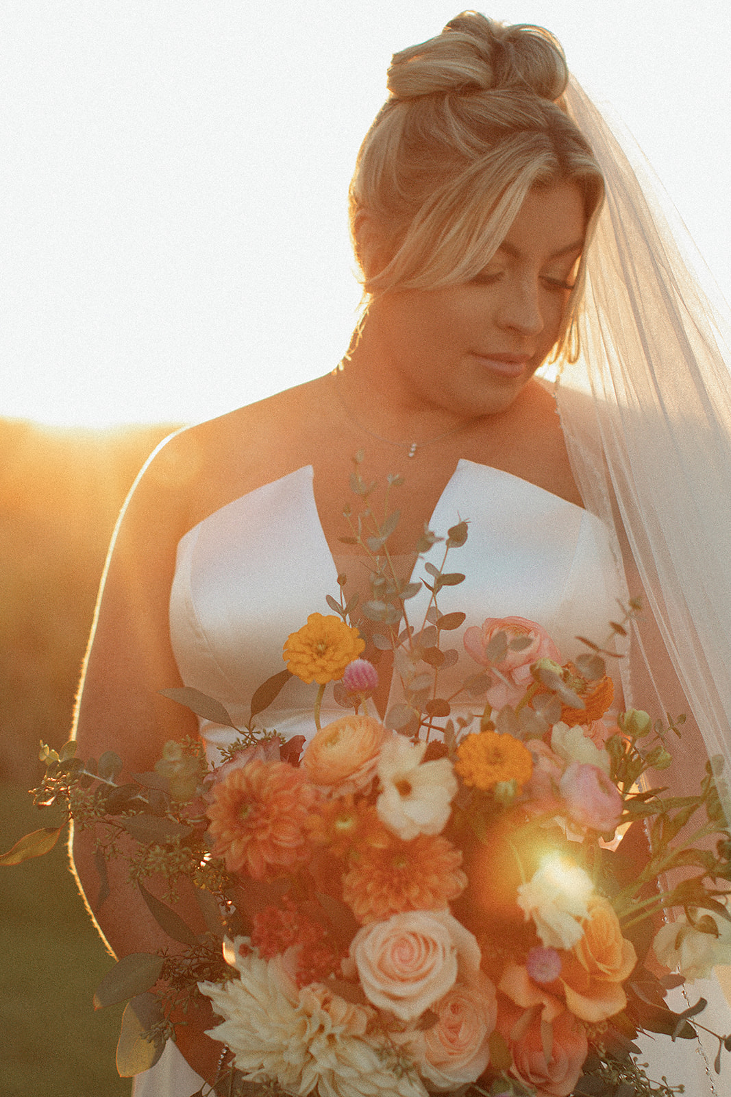 Charlottesville wedding photographer captures sunset wedding pictures with bride holding her floral bouquet and looking down 