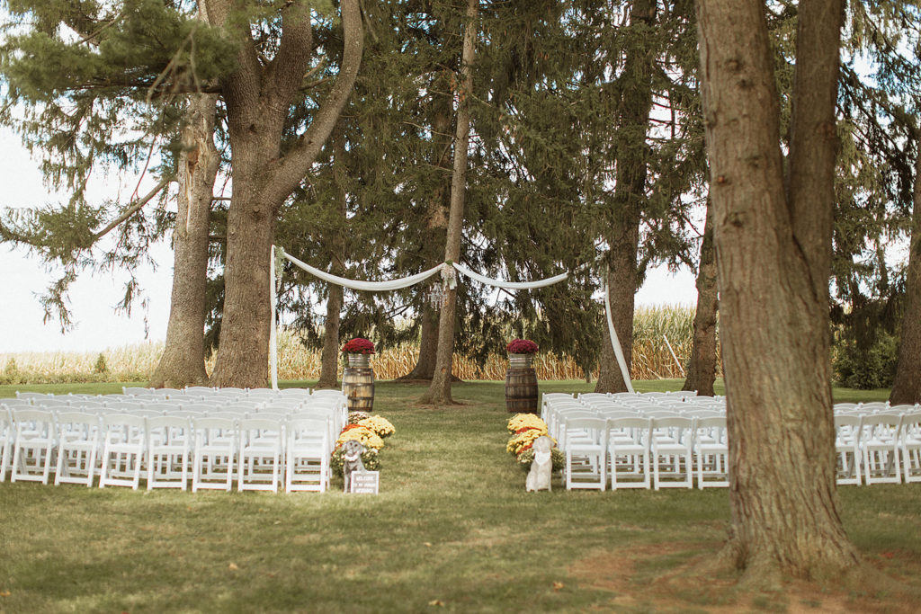 outdoor ceremony space at a Virginia wedding venue with white fold up chairs, fall florals and tall trees captured by Richmond wedding photographer