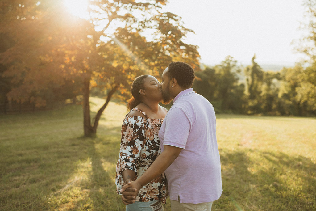 outdoor engagement photos with Charlottesville wedding photographer, man and woman holding hands and kissing while standing in a field at sunset