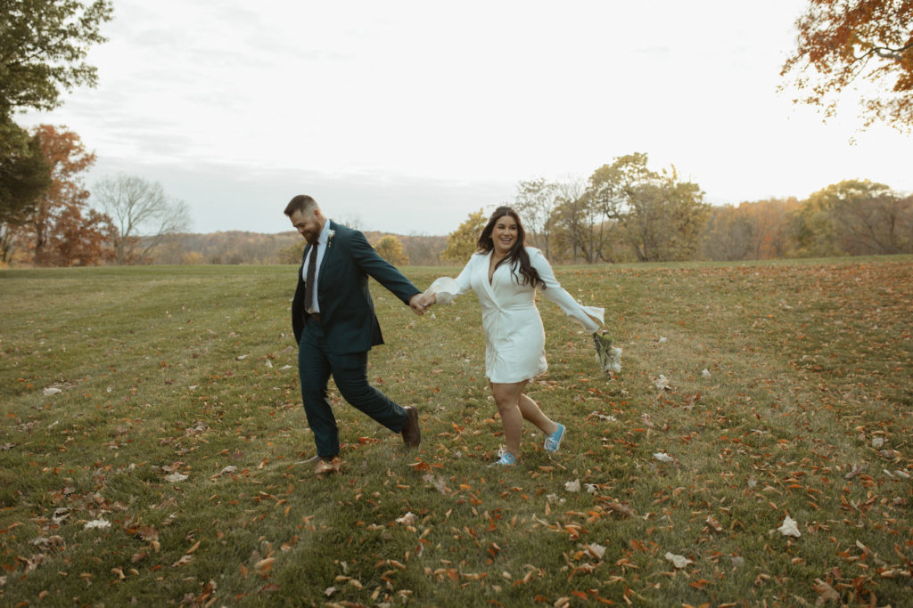 bride and groom holding hands and running through a field captured by Virginia wedding photographer