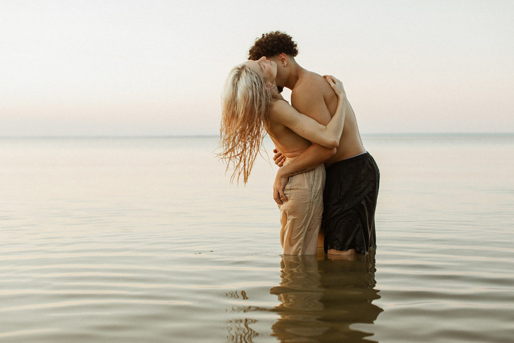 A fun and sexy engagement shoot for a couple at Westmoreland state park | standing in the water, no tops, hugging.