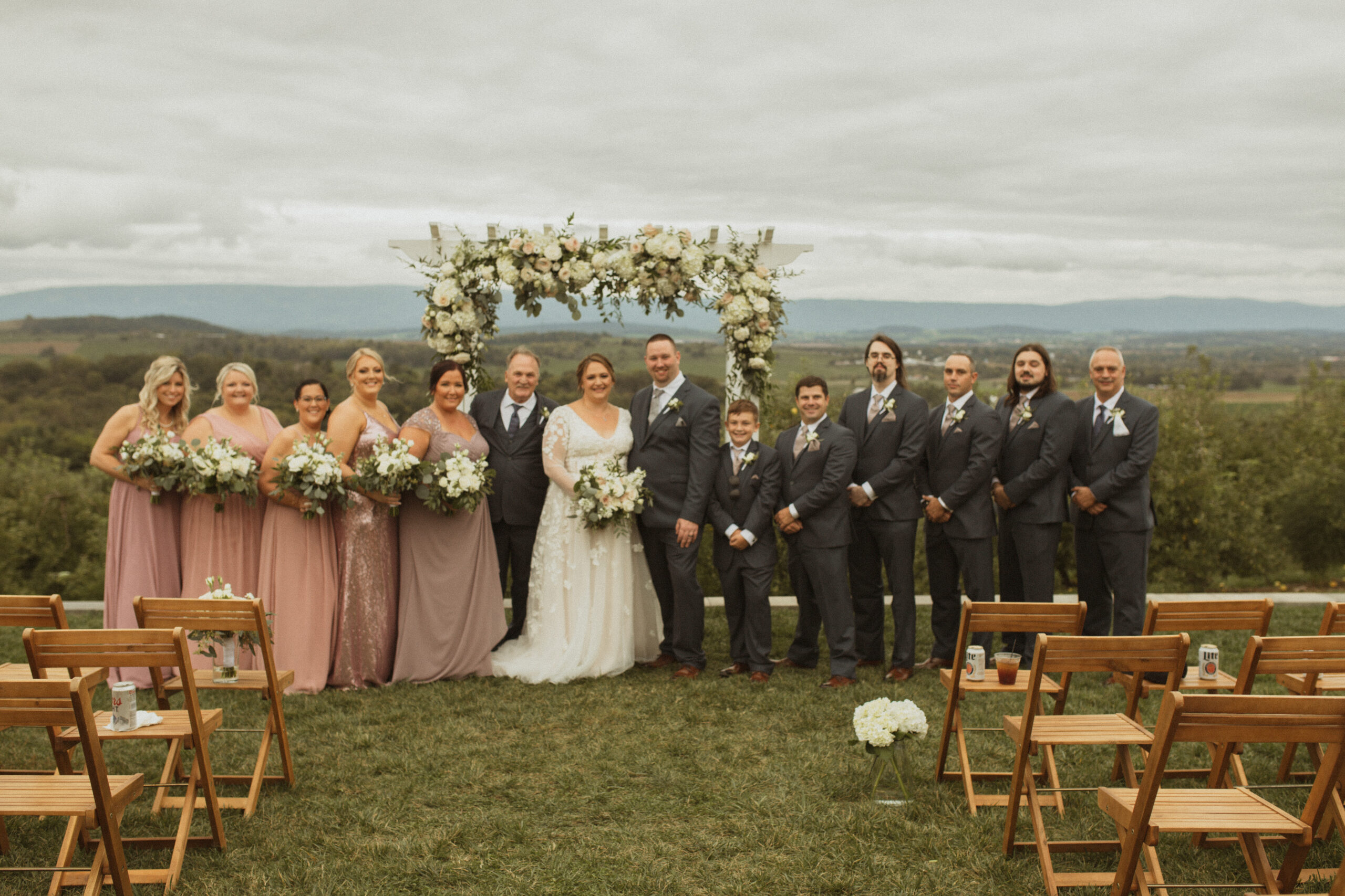 Entire wedding party of both sides standing in front of the flower arch for a group photo