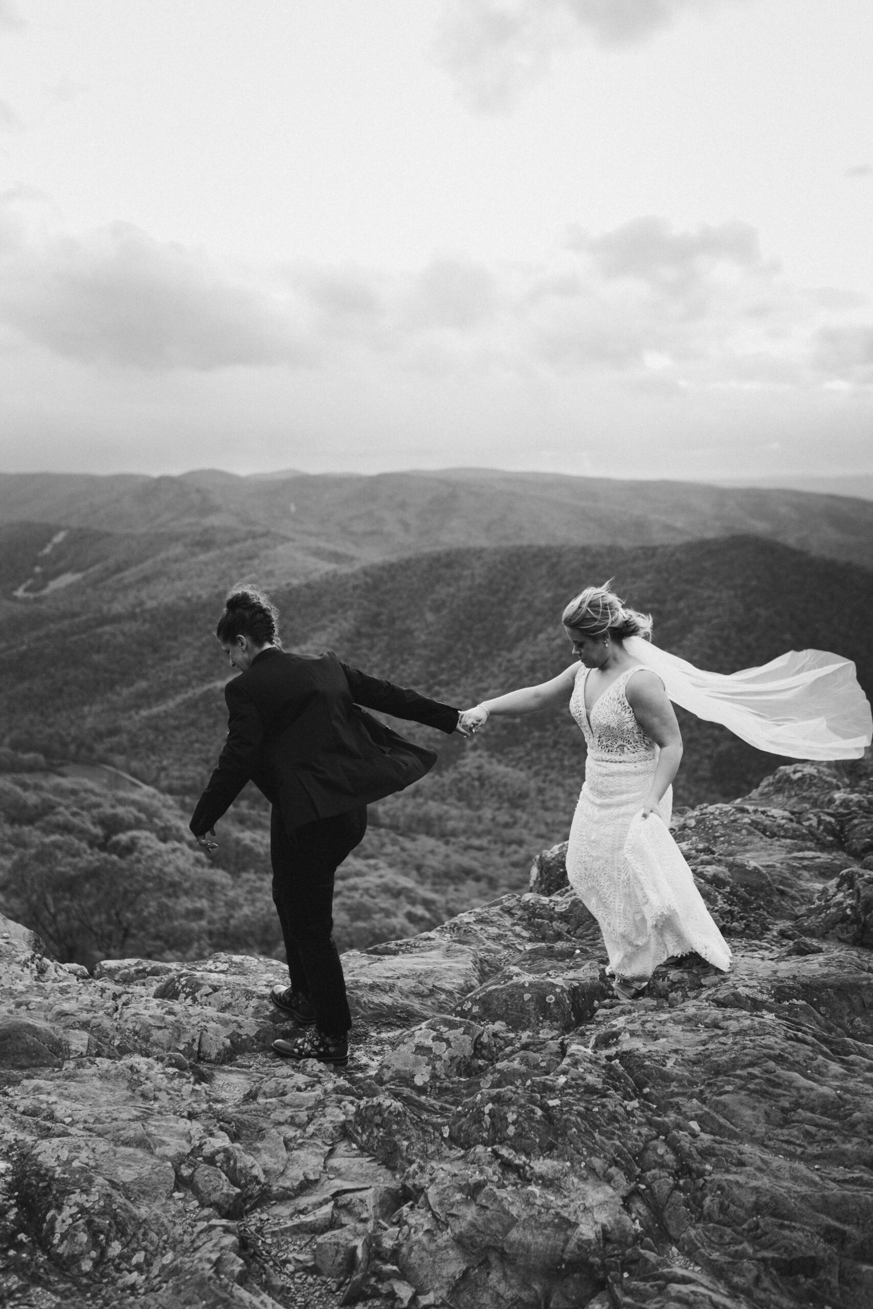 Same-sex couple walking across the mountain overlook holding hands after Shenandoah National Park elopement