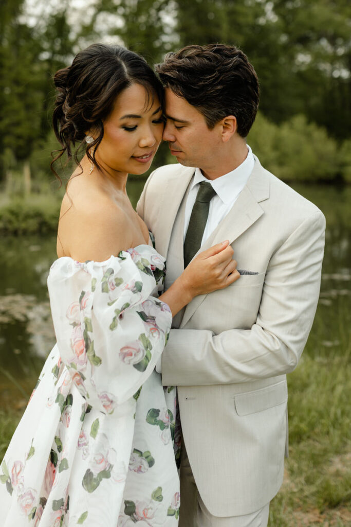 Couples standing close, forehead to forehead. She is wearing a white gown with pink and green flowers, while he is wearing a 3 piece suit in beige with a green tie.