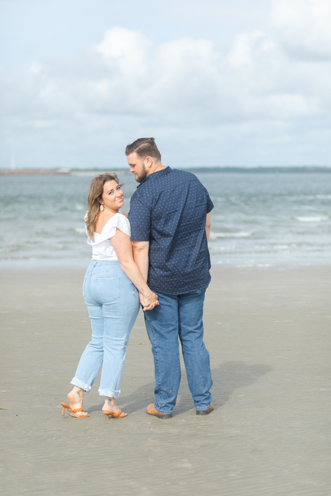 Couple standing in front of the beach water holding hands looking back at the camera