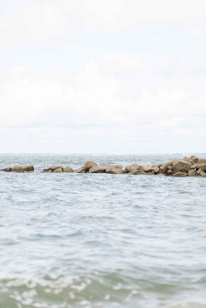 Calm ocean waters meet a rocky breakwater at Sullivan's Island, setting a serene scene perfect for engagement photos.