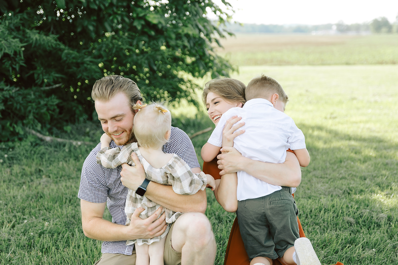 Young Family hugging in a field in front of a tree