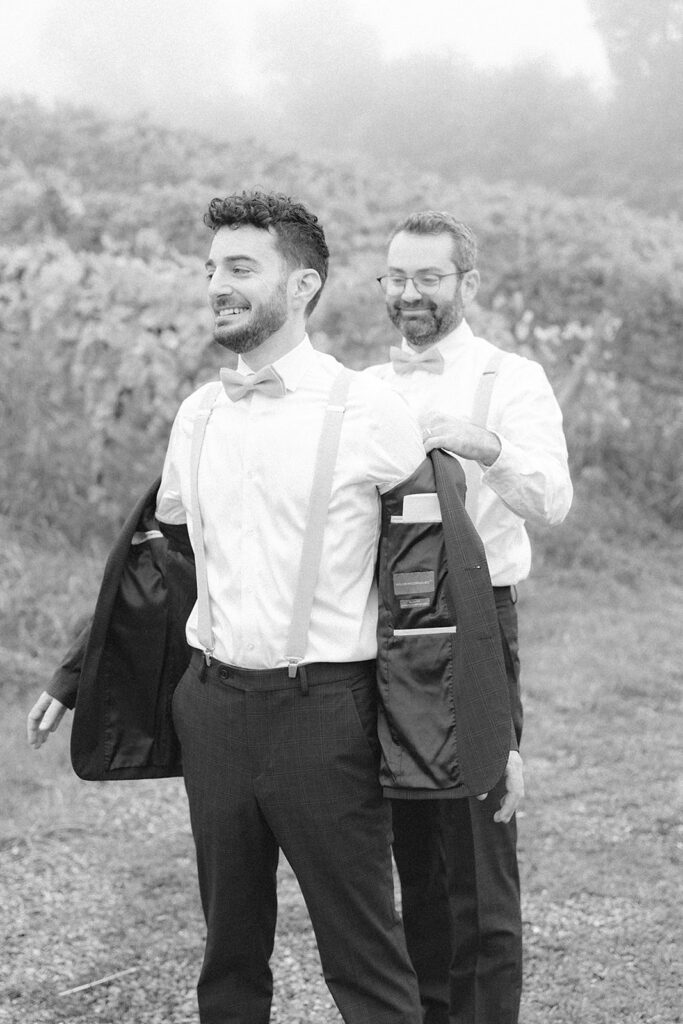 Groom getting ready outdoors with the help of a groomsman on a misty day at Bluemont Vineyard.