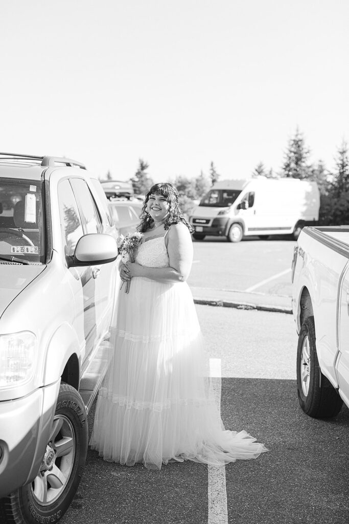 Estella, holding her bouquet and smiling, stands in the parking lot of Cadillac Mountain moments before her elopement ceremony in Acadia National Park