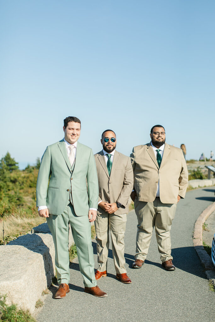 Calvin with his groomsmen at Acadia National Park, all dressed in coordinated suits under the clear blue sky