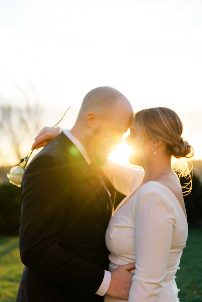 Couple embracing during sunset at Chatham Manor, with golden sunlight streaming between them, creating a romantic glow