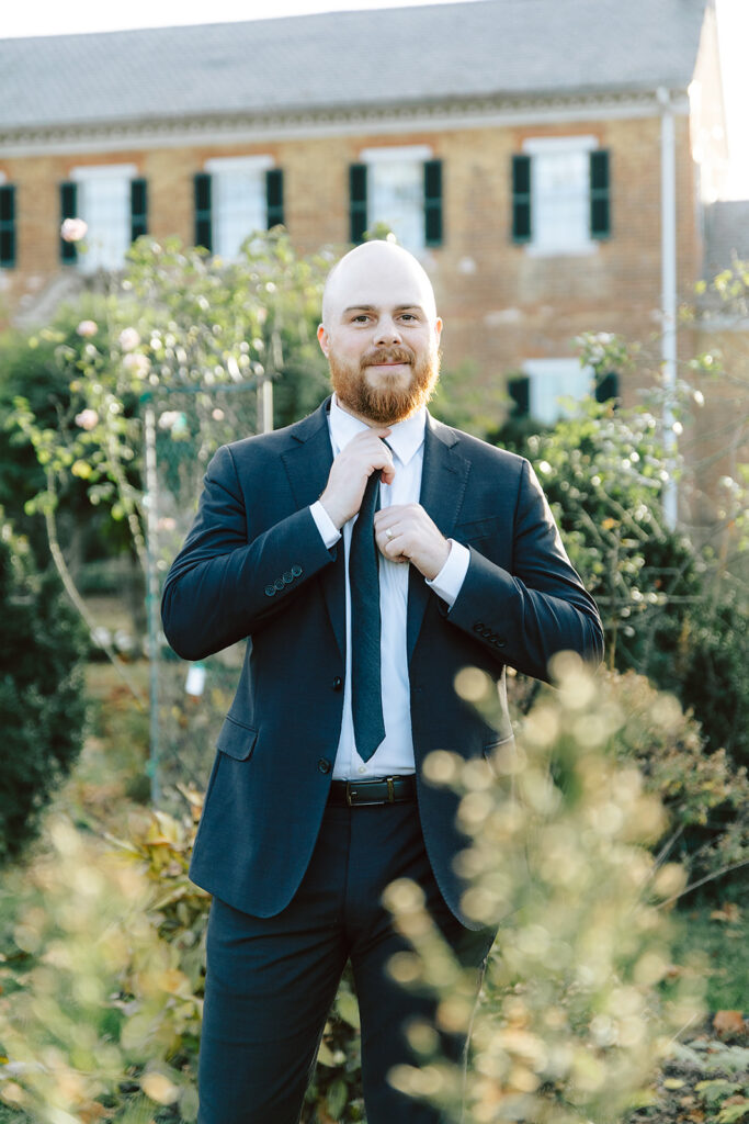 Man in a black suit adjusting his tie in the garden 