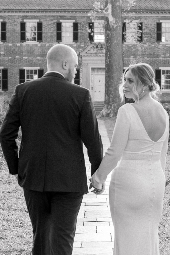 A black and white photo of a couple holding hands while walking toward Chatham Manor in Fredericksburg, Virginia, with the historic building in the background.