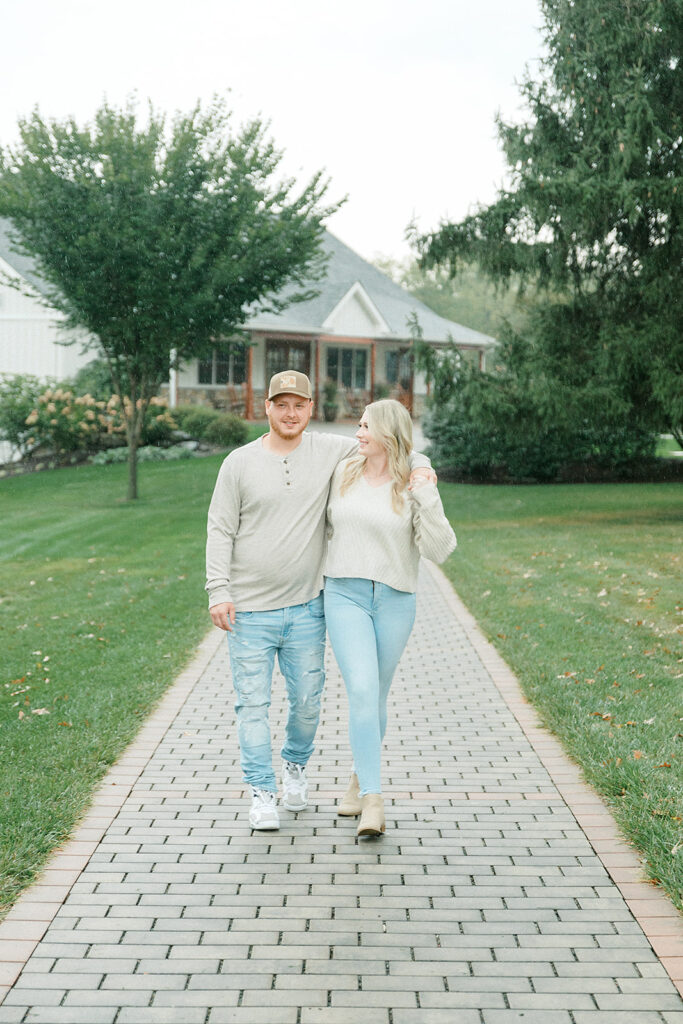 A couple walking arm-in-arm on a brick pathway surrounded by green lawns at Drumore Estate during their engagement session.