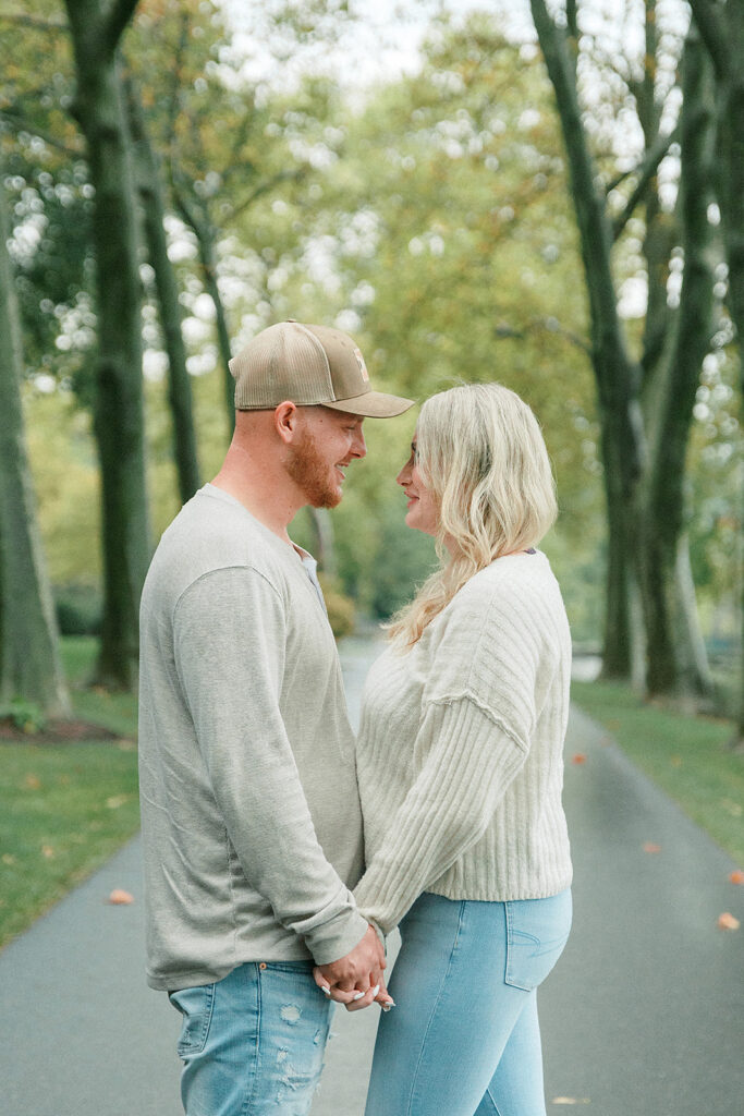 Romantic moment of a couple holding hands and gazing at each other on a peaceful path surrounded by trees.