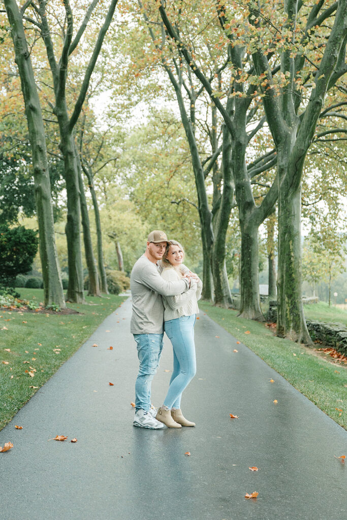 Couple embracing on a tree-lined path during their engagement session at a scenic estate.