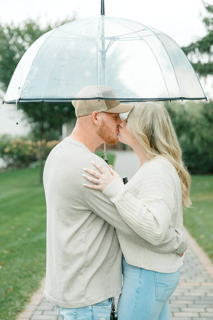 A couple sharing a kiss under a clear umbrella during their rainy engagement session at Drumore Estate.