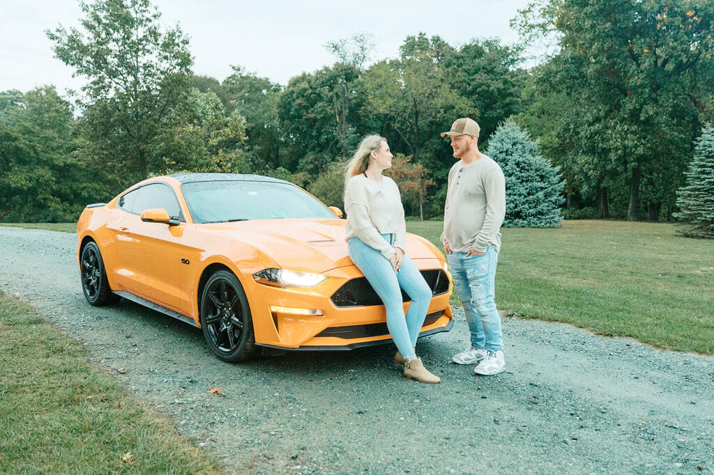 Couple standing next to a bright orange Mustang during their engagement session at Drumore Estate in Lancaster, PA.