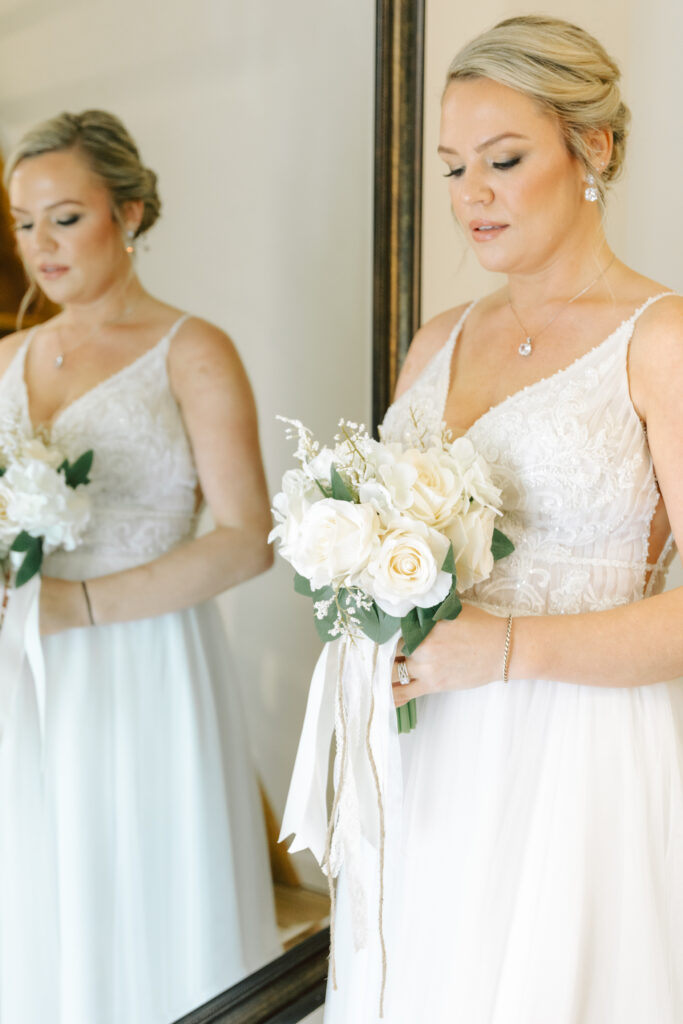 Bride holding her bouquet in front of a mirror at Layz S Ranch, showcasing her lace wedding gown before the ceremony.