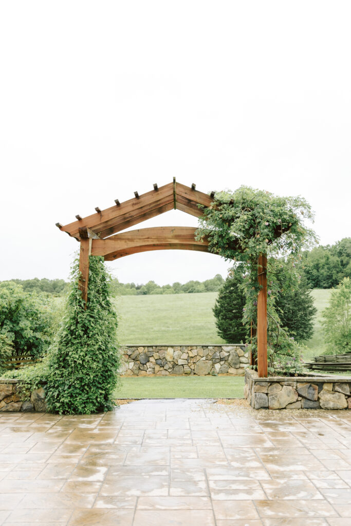 Ceremony arbor at Layz S Ranch adorned with greenery, overlooking scenic fields and stone walls in Fluvanna County, Virginia.