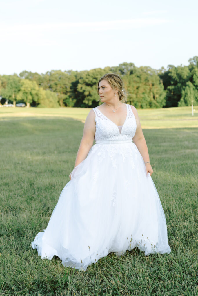 Bride poses elegantly in her lace wedding gown, standing in the open fields at Bowles Farm with the Southern Maryland countryside in the background.