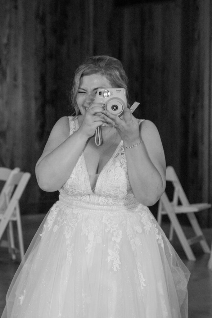 Bride shares a playful moment capturing a photo with a Polaroid camera during her Bowles Farm wedding reception.