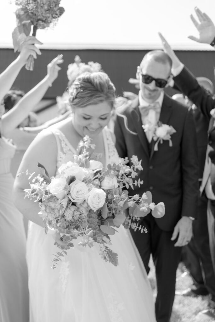 Bride smiles while holding her bouquet during a joyful wedding recessional at Bowles Farm, surrounded by celebrating family and friends.