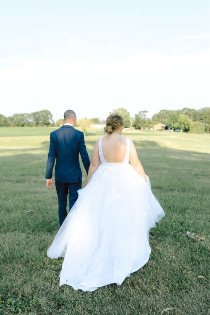 Bride and groom walk hand-in-hand across the open fields at Bowles Farm, capturing a quiet, romantic moment on their wedding day.