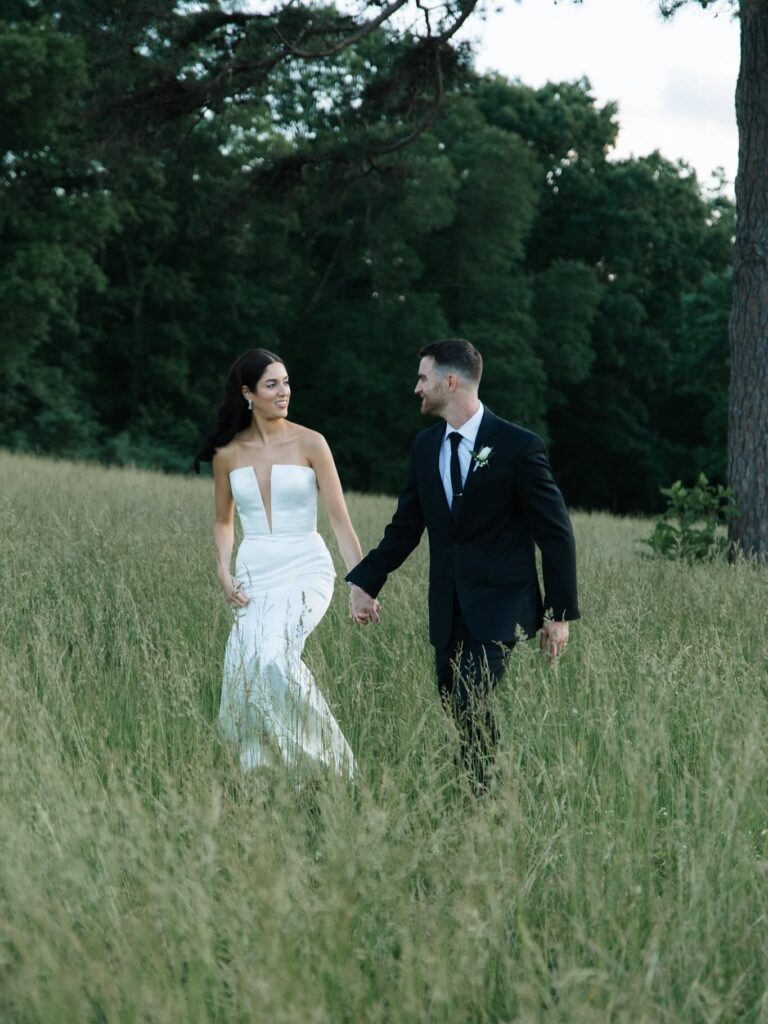 Bride and groom walking through field at Virginia barn wedding venue

