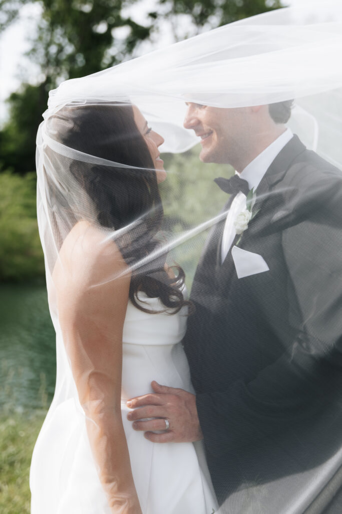 Romantic close-up of bride and groom smiling under the veil with soft light highlighting their expressions.
