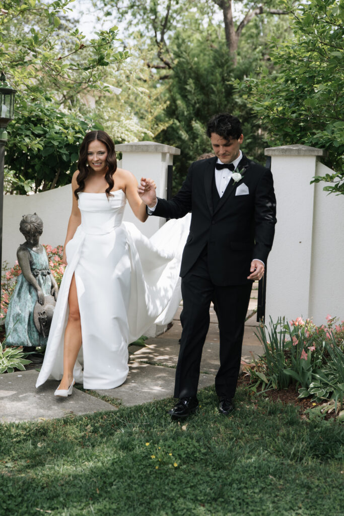 Bride and groom walking hand-in-hand through Morais Vineyards garden pathway, surrounded by spring flowers.
