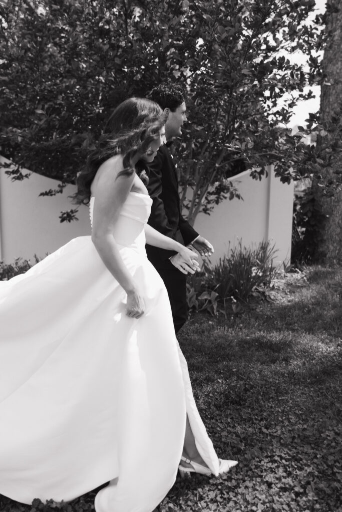 Bride and groom walking side-by-side through grass, captured in soft black and white for a timeless look.

