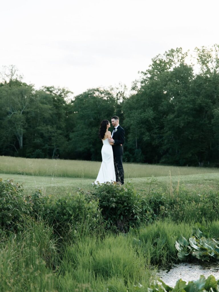 Couple standing on the green next to a small lake in an open field in virginia