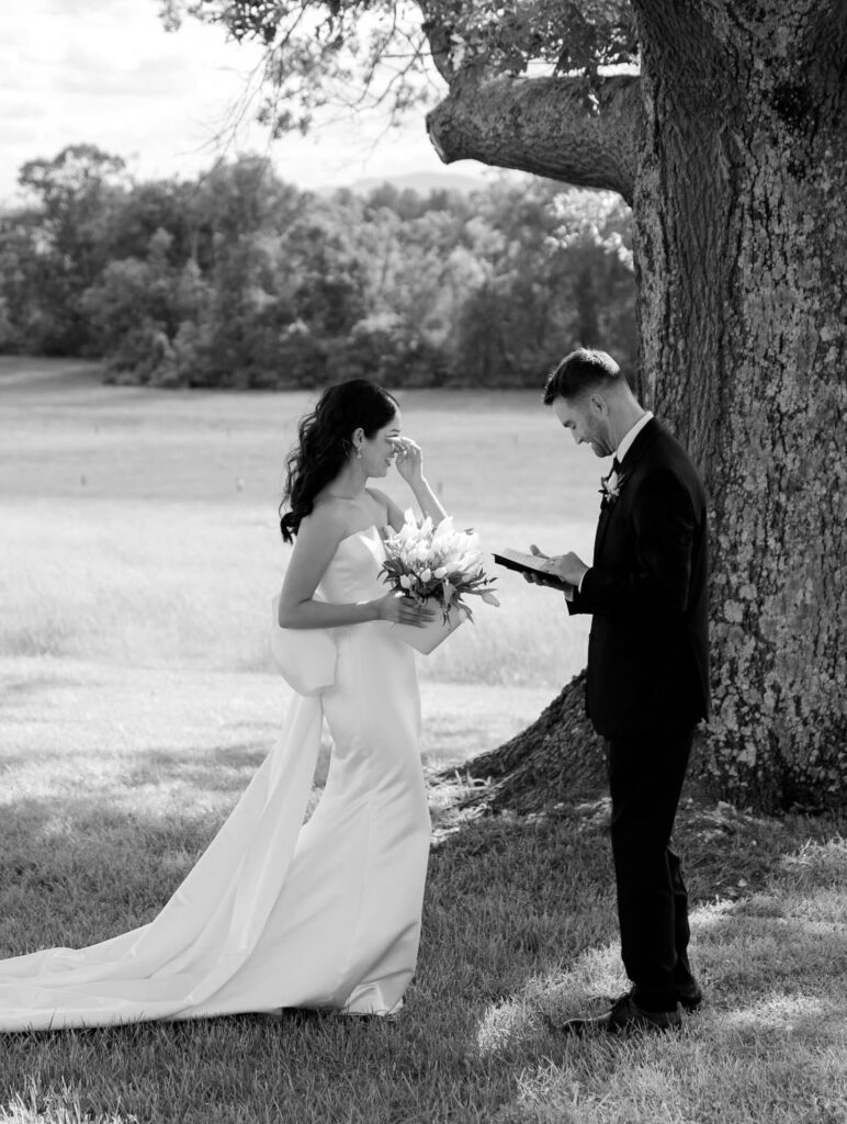 Bride and groom exchanging vows under tree at barn wedding venue in Virgin

